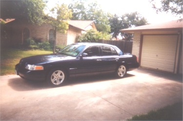 2002 Ford Crown Victoria - Dark blue 2002 Ford Crown Victoria sedan parked on a concrete driveway next to a garage.
