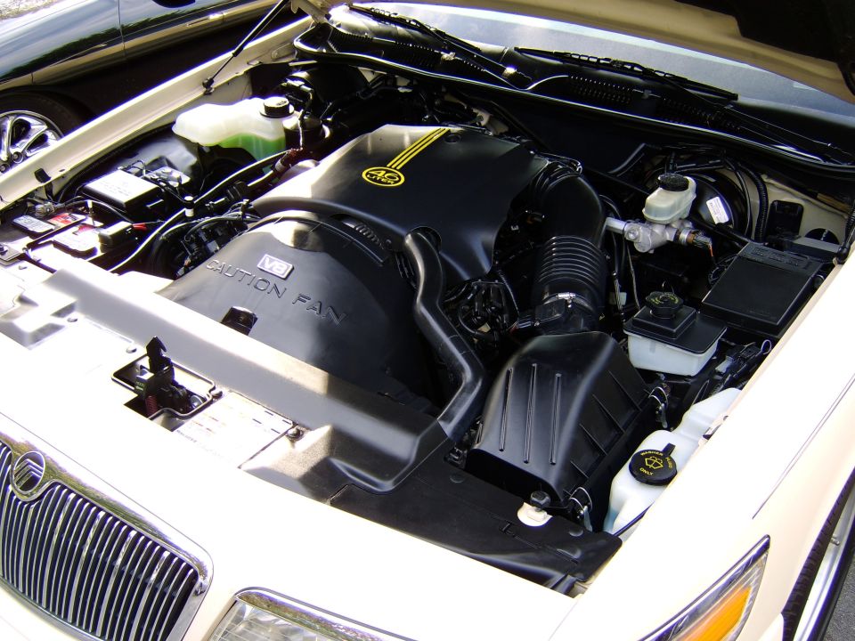 White car engine bay with black V8 cover reading CAUTION FAN and 4.6 badge