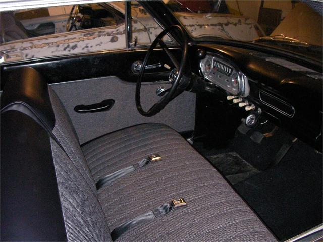 Vintage Ford Falcon interior with gray bench seat, steering wheel and dashboard