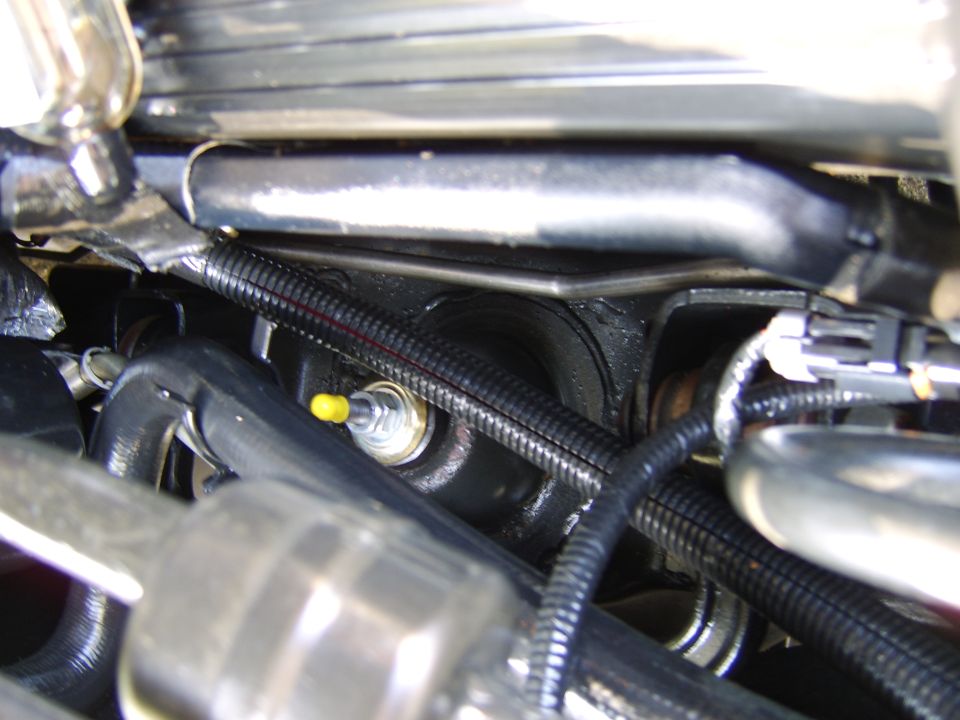Engine bay close-up with metal fitting, black wiring looms and hoses