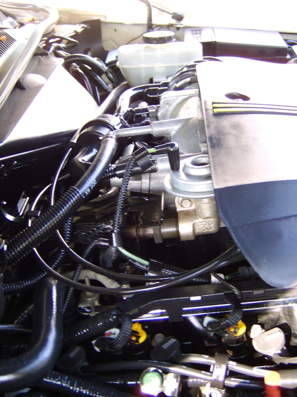 Engine bay close-up of throttle body, EGR valve, fuel rail and wiring under a black engine cover