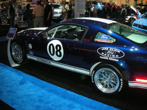 1998 Ford Crown Victoria - dark blue Ford Mustang Cobra race car wearing number 08 and Jim Click Ford Racing livery sits on a blue carpet.