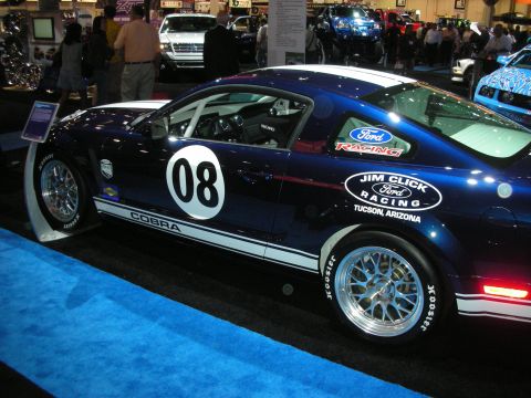 1998 Ford Crown Victoria - Side profile of a dark blue Ford Mustang Cobra race car numbered 08 with Jim Click Ford Racing decals on a show floor.
