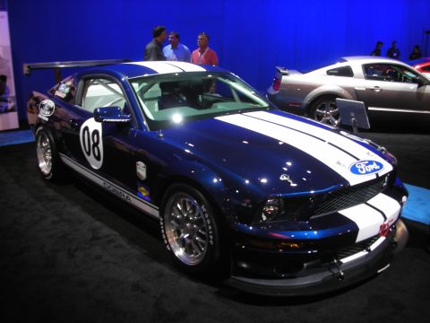 1998 Ford Crown Victoria - dark blue Ford Mustang Cobra race car with white stripes, rear wing and number 08 displayed under blue lighting.