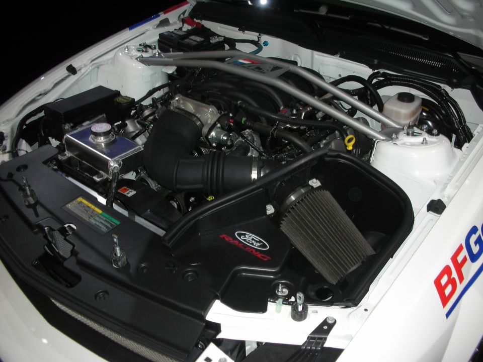 Engine bay of white race car with Ford Racing cold-air intake and strut brace