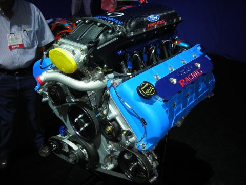 1998 Ford Crown Victoria - blue-and-silver Ford Racing V8 crate engine with a carbon-fiber intake displayed on a stand at a show.