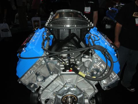 1998 Ford Crown Victoria - blue Ford Racing V8 engine topped with a carbon-fiber intake manifold sits on a display stand at an indoor show.