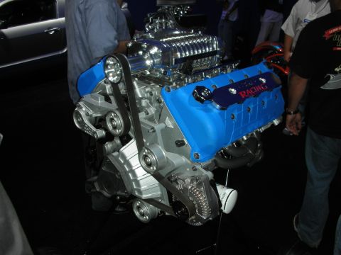 1998 Ford Crown Victoria - blue Ford Racing V8 engine topped with a polished supercharger sits on a stand at a crowded show.