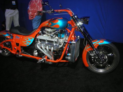 1998 Ford Crown Victoria - custom chopper motorcycle with orange-and-blue flame paint and exposed V-twin engine stands against a blue backdrop.