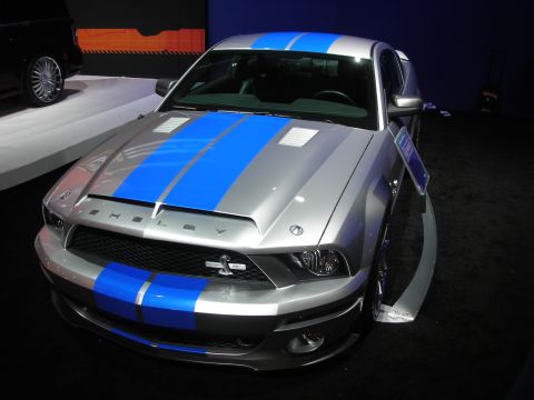 Silver Shelby Mustang with blue racing stripes front view under show lights