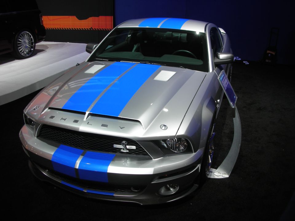 Silver Shelby Mustang with blue racing stripes front view under show lights