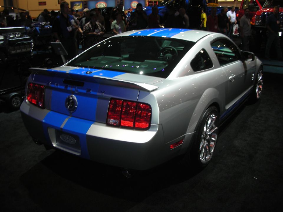 Rear three-quarter of silver Shelby Mustang with blue stripes at auto show