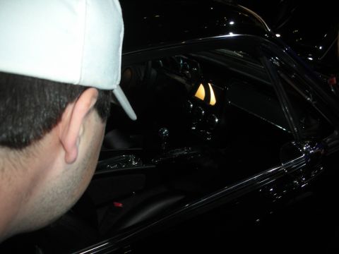 Man in white cap peering through window into dark car interior with roll cage