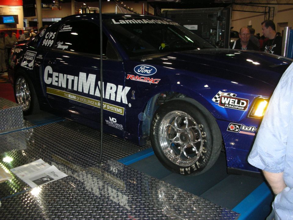 Blue CentiMark-sponsored Ford drag car with chrome Weld wheels on display