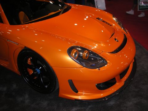 Front detail of an orange sports car with black wheels and carbon splitter