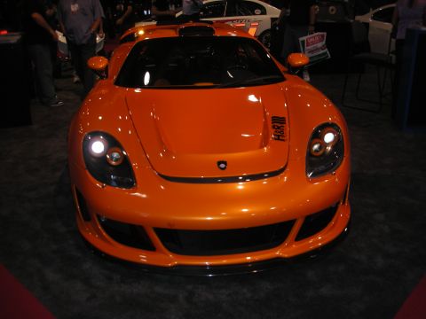 Front view of an orange mid-engine sports car at an auto show