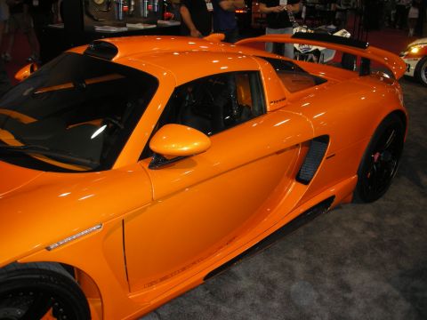 Side view of an orange mid-engine coupe with rear wing and black wheels