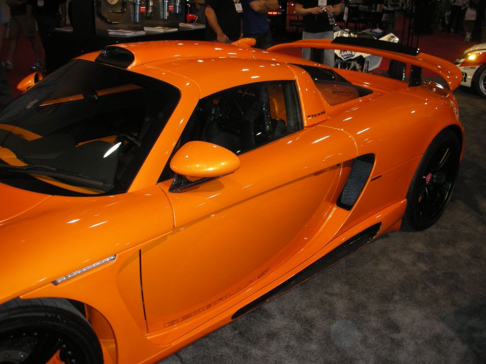 Side view of an orange mid-engine coupe with rear wing and black wheels