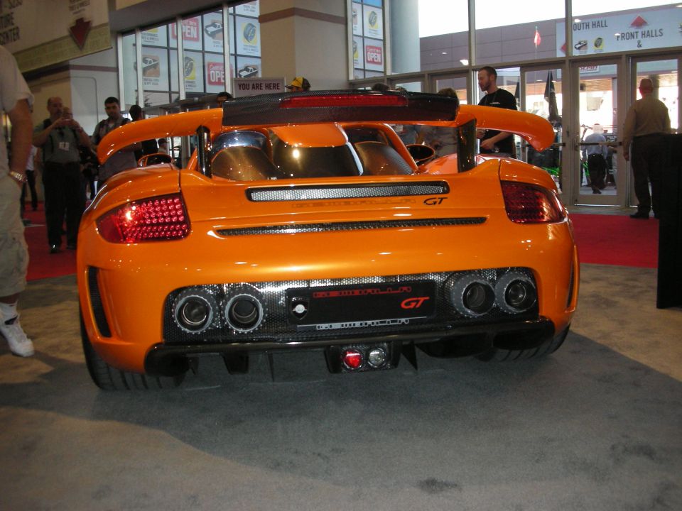 Rear of an orange GT car with carbon diffuser and quad exhaust at a convention