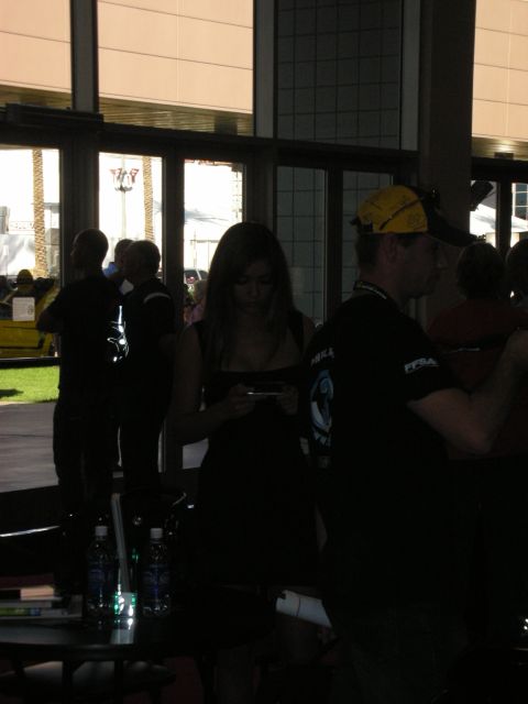 Woman in black dress checking phone among people in a dim convention lobby