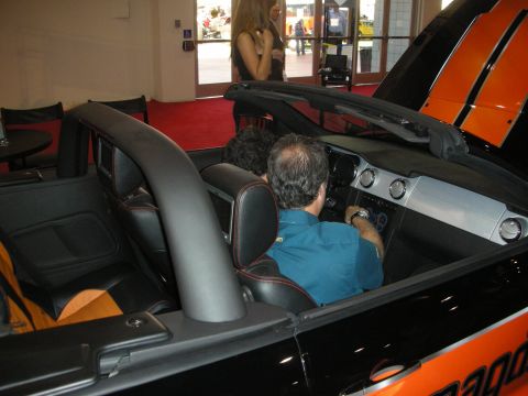 Man sitting in an orange and black convertible at an indoor show