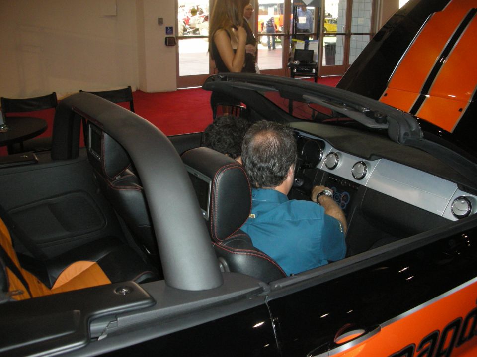 Man sitting in an orange and black convertible at an indoor show