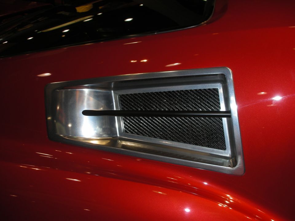 Polished chrome hood scoop with carbon-fiber mesh insert on a glossy red car body