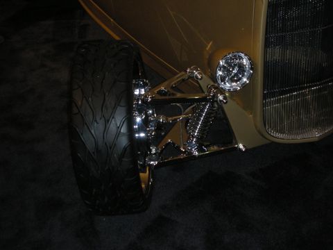 Front suspension and wheel of a gold hot rod with chrome shock and headlight