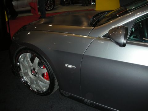 Front fender and chrome wheel of a silver sports car with red brake caliper at a show