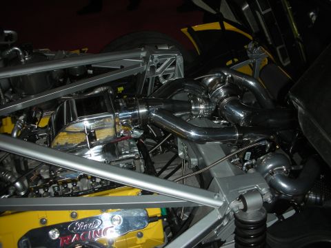 Polished twin-turbo engine in a yellow tube-frame chassis with Ford Racing cover