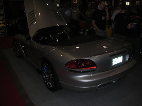 Rear three-quarter of a silver convertible roadster with open hood at a car show
