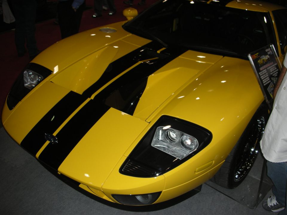 Front of a yellow Ford GT with black racing stripes at an indoor car show