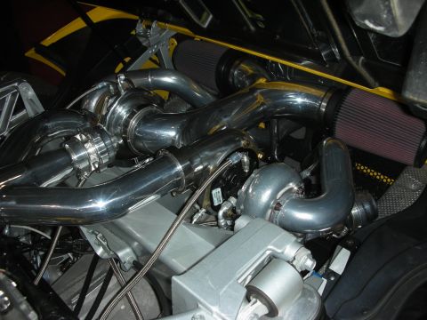 Polished twin-turbo plumbing and intercooler piping inside a yellow engine bay