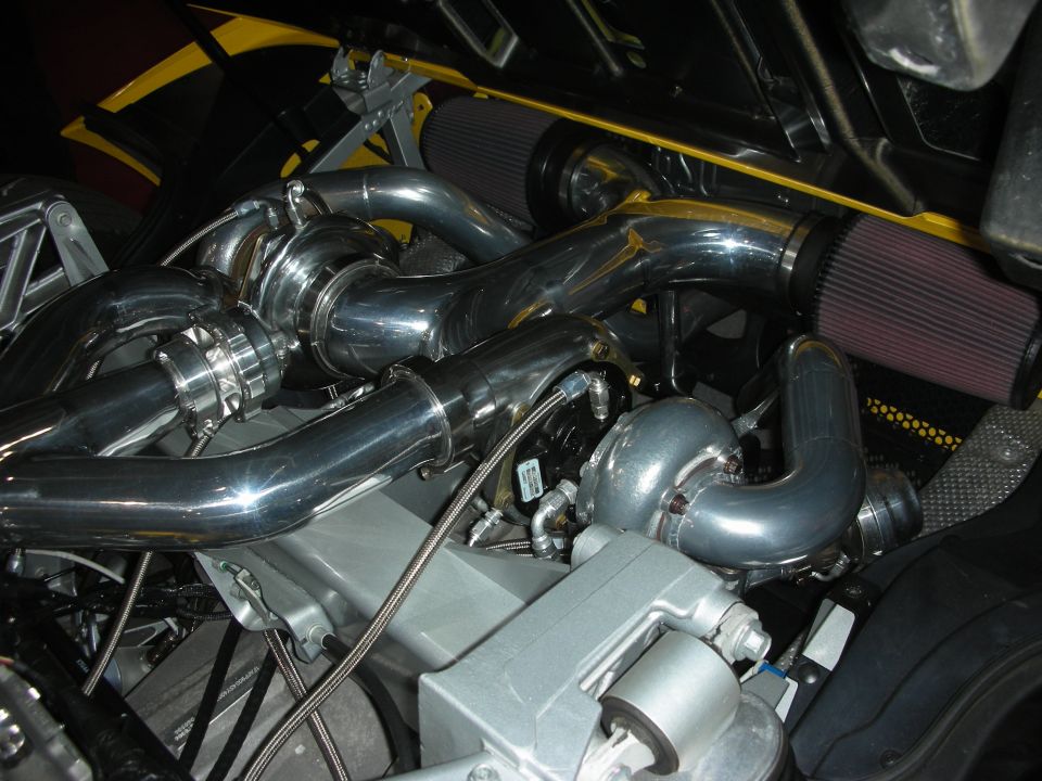 Polished twin-turbo plumbing and intercooler piping inside a yellow engine bay