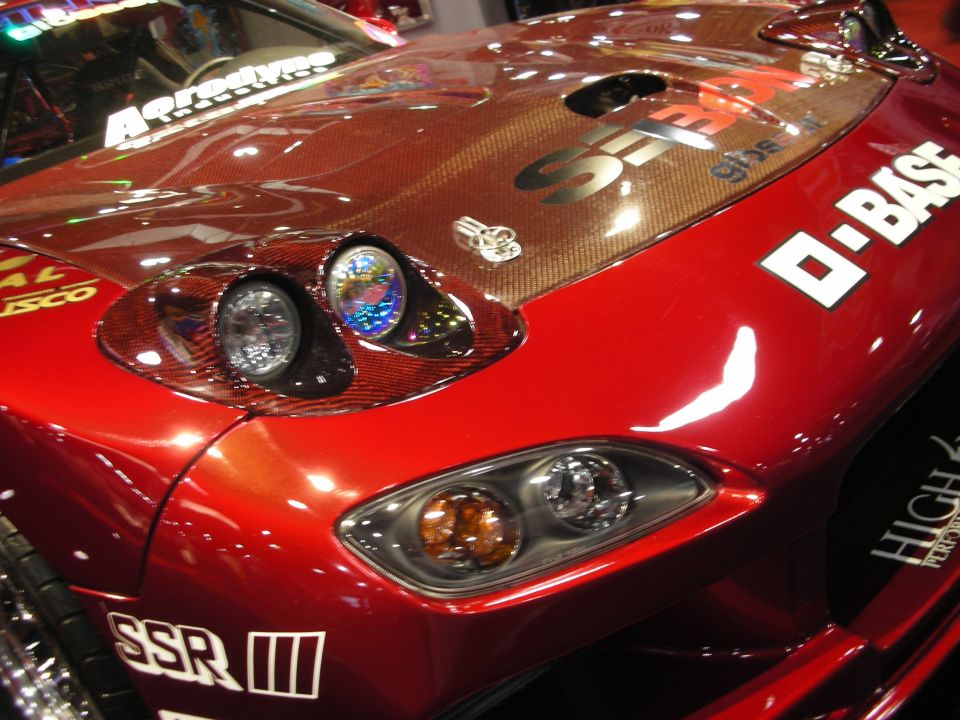Close-up of a red coupe's carbon hood, gauges, and headlights with sponsor decals
