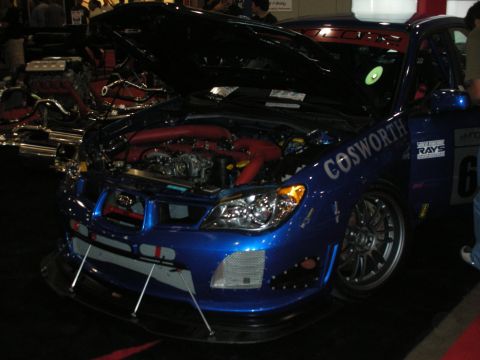 Blue tuner race car with open hood, red intake piping, and Cosworth livery