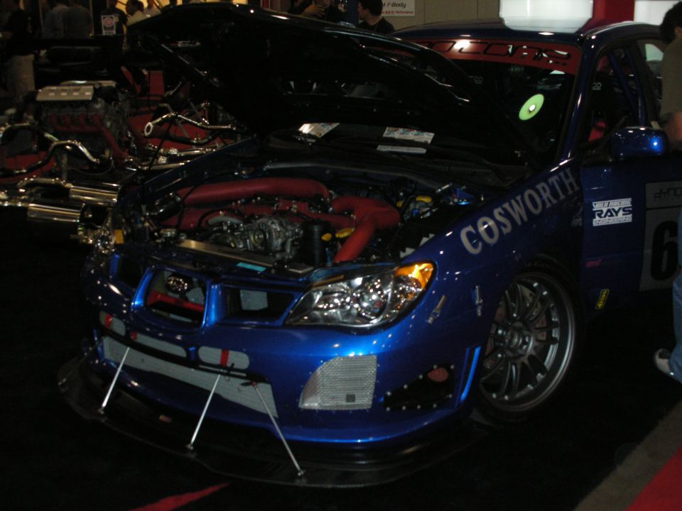 Blue tuner race car with open hood, red intake piping, and Cosworth livery