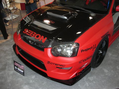 Front of red and black Subaru WRX STI with Seibon carbon hood and sponsor decals