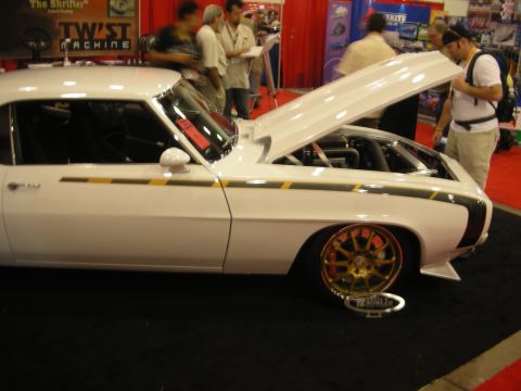 White custom Camaro with gold wheels and open hood at busy indoor show