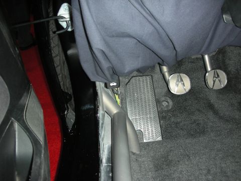Driver footwell of custom car showing pedals and rubber floor mat