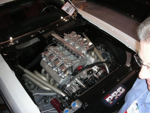 1998 Ford Crown Victoria - highly polished V8 engine with a tall ribbed aluminum intake sits in an open engine bay as a man looks on at an indoor show.