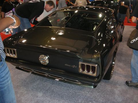 1998 Ford Crown Victoria - Rear three-quarter view of a glossy black fastback muscle car with sequential-style taillights, surrounded by people at a show.