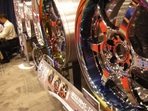1998 Ford Crown Victoria - row of oversized polished and iridescent alloy wheels on a trade-show stand, with a Williams banner along the front.