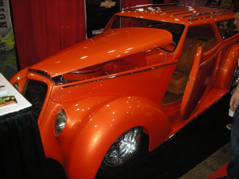1998 Ford Crown Victoria - orange custom hot rod with a roof rack and suicide door open, revealing a tan leather interior, displayed at a show.