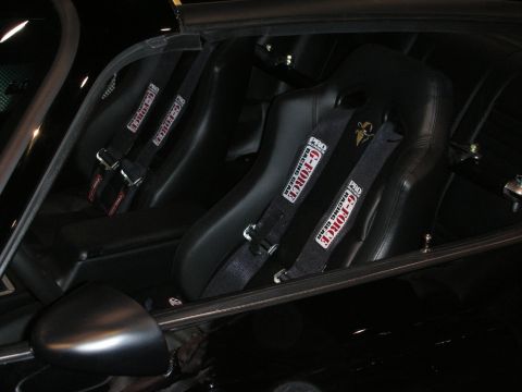 1998 Ford Crown Victoria - Two black racing bucket seats fitted with Crow brand five-point harnesses inside a dark custom car interior.