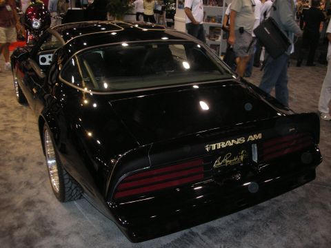 1998 Ford Crown Victoria - Rear three-quarter view of a black Pontiac Trans Am with gold Trans Am lettering and ribbed taillights at a crowded show.