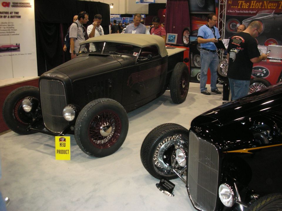 Two early Ford hot rods, a black roadster and black coupe, on a show floor