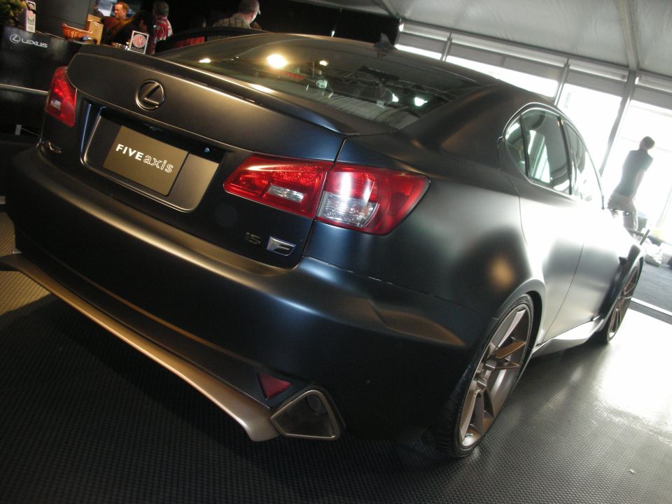 Rear view of matte-black Lexus coupe with Five Axis plate at an indoor show