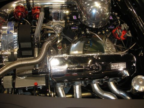 1998 Ford Crown Victoria - Detailed engine close-up showing a chrome 'KMF' valve cover, red distributor cap, braided lines and polished intake plumbing.