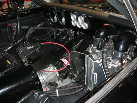 1998 Ford Crown Victoria - Bare race-car interior showing a small steering wheel, round gauge cluster, shifter and engine plumbing intruding into the cabin.